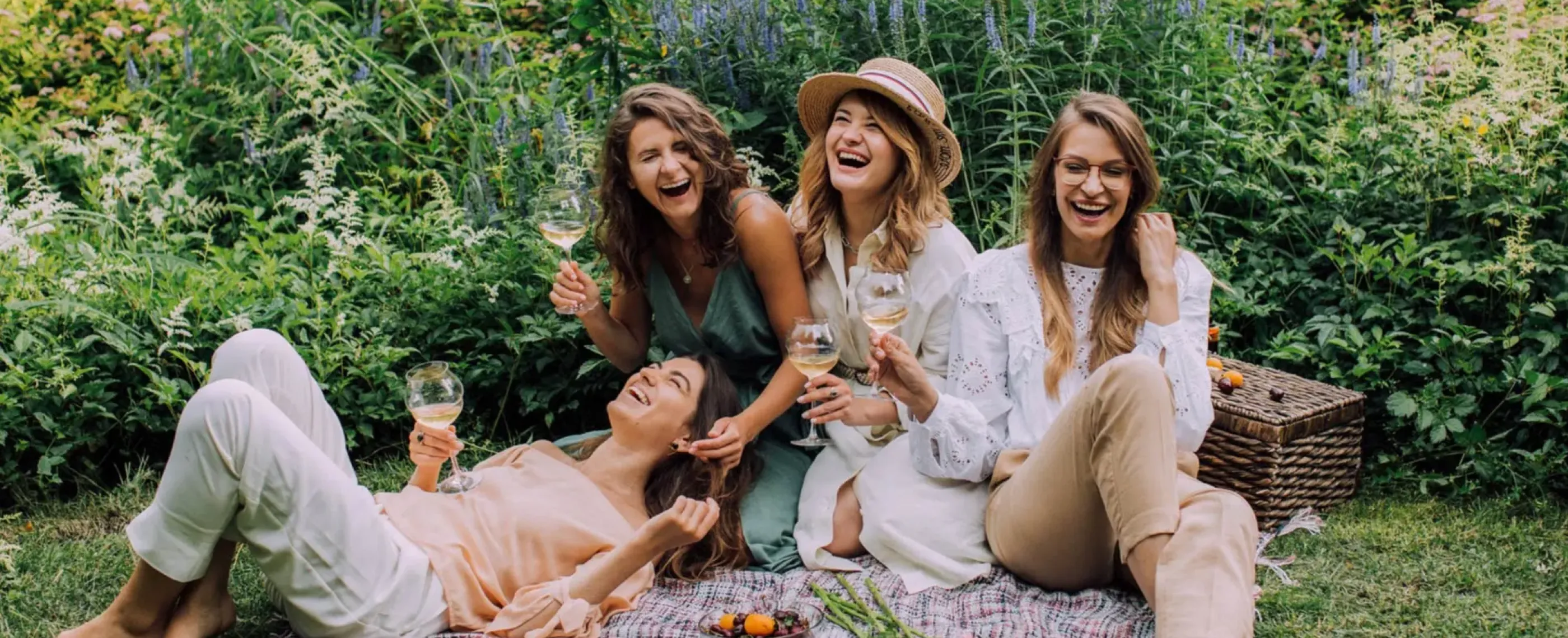 Ladies on a picnic blanket laughing and drinking wine