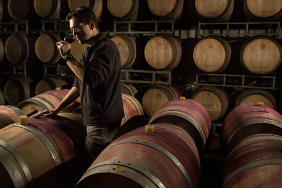A person in a cellar tasting wine surrounded by barrels