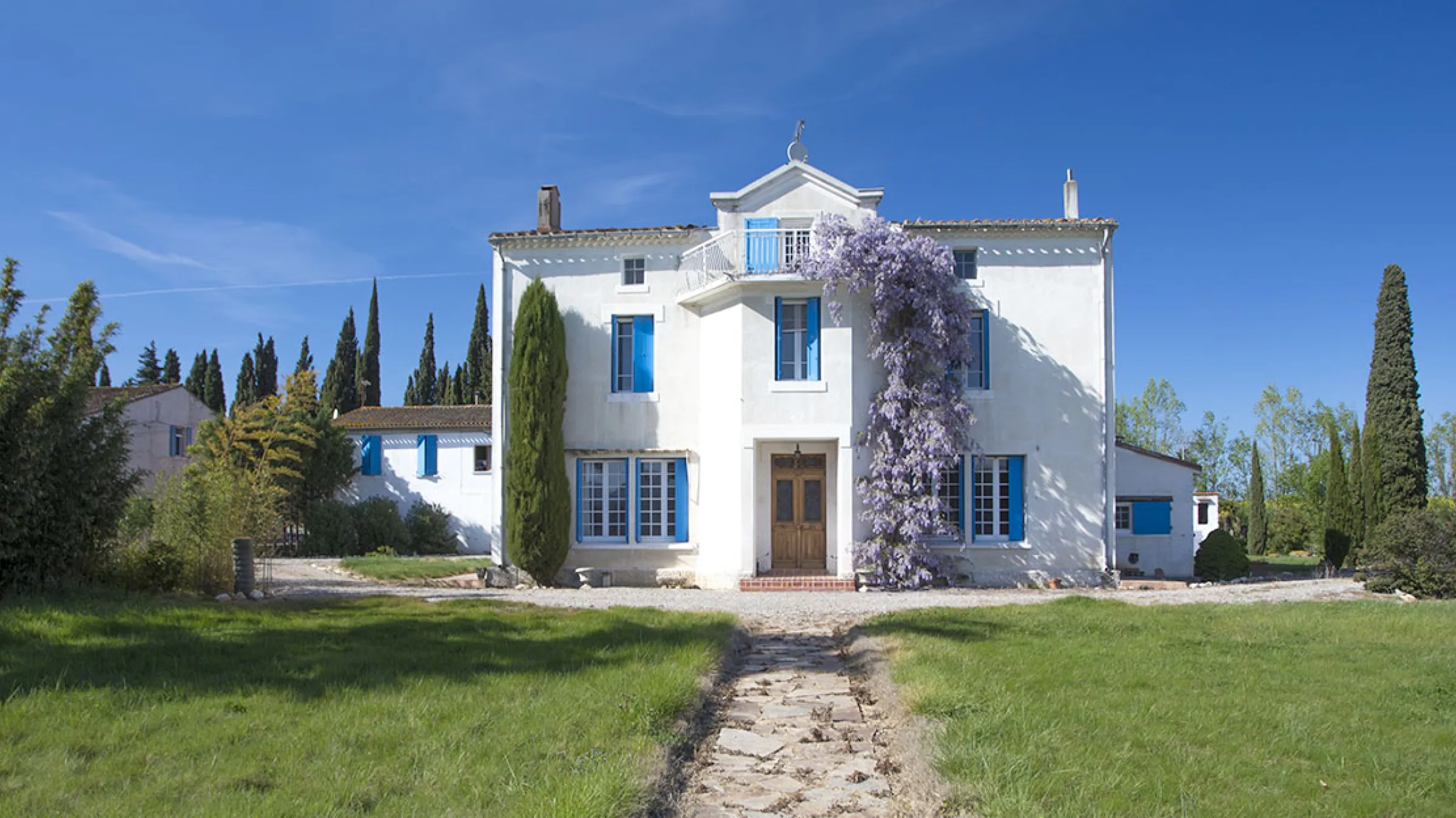 Front view of a white house with blue windows, brown door and grass